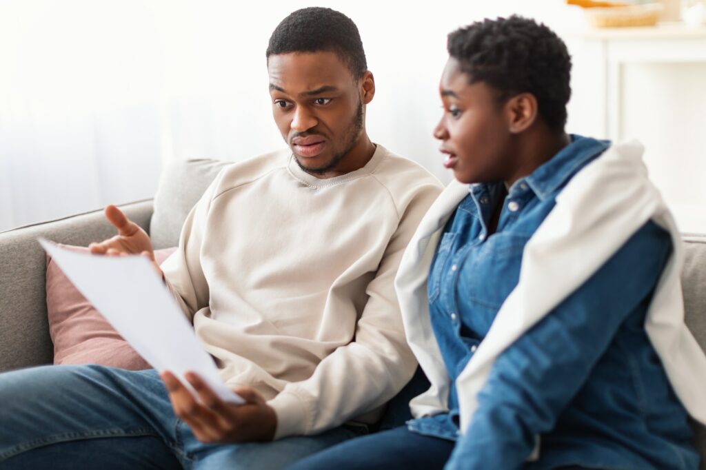 Confused afro couple reading documentation at home, sitting on couch