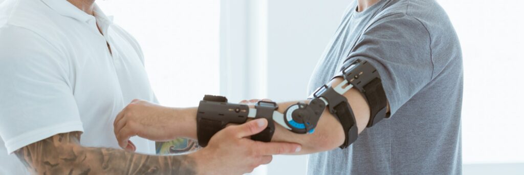 Tattooed physiotherapist who puts an orthosis on the hand of a young patient after an accident