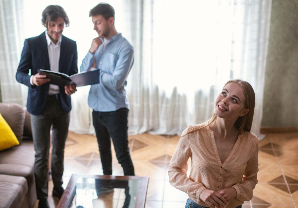 Young lady looking at new house while her husband and real estate agent discussing ownership